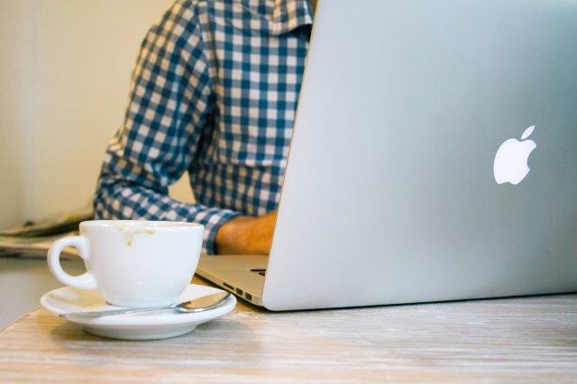 a desk setop with a laptop, cup of coffee and a person who coudl be researching information on a short code