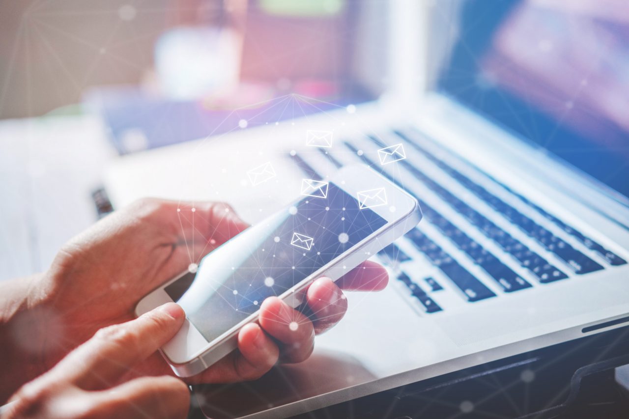 Man holding a phone with a laptop background